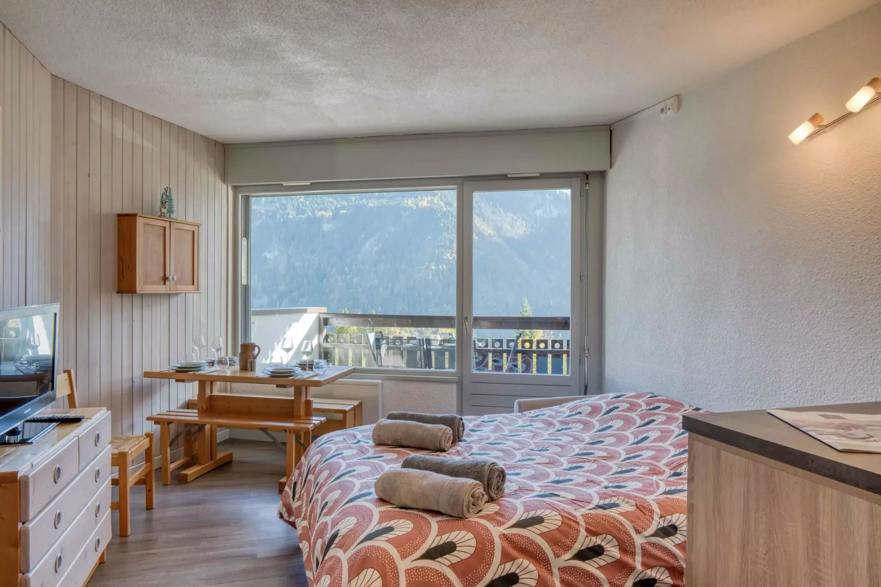 A bedroom with a patterned bed and large windows overlooking a balcony.