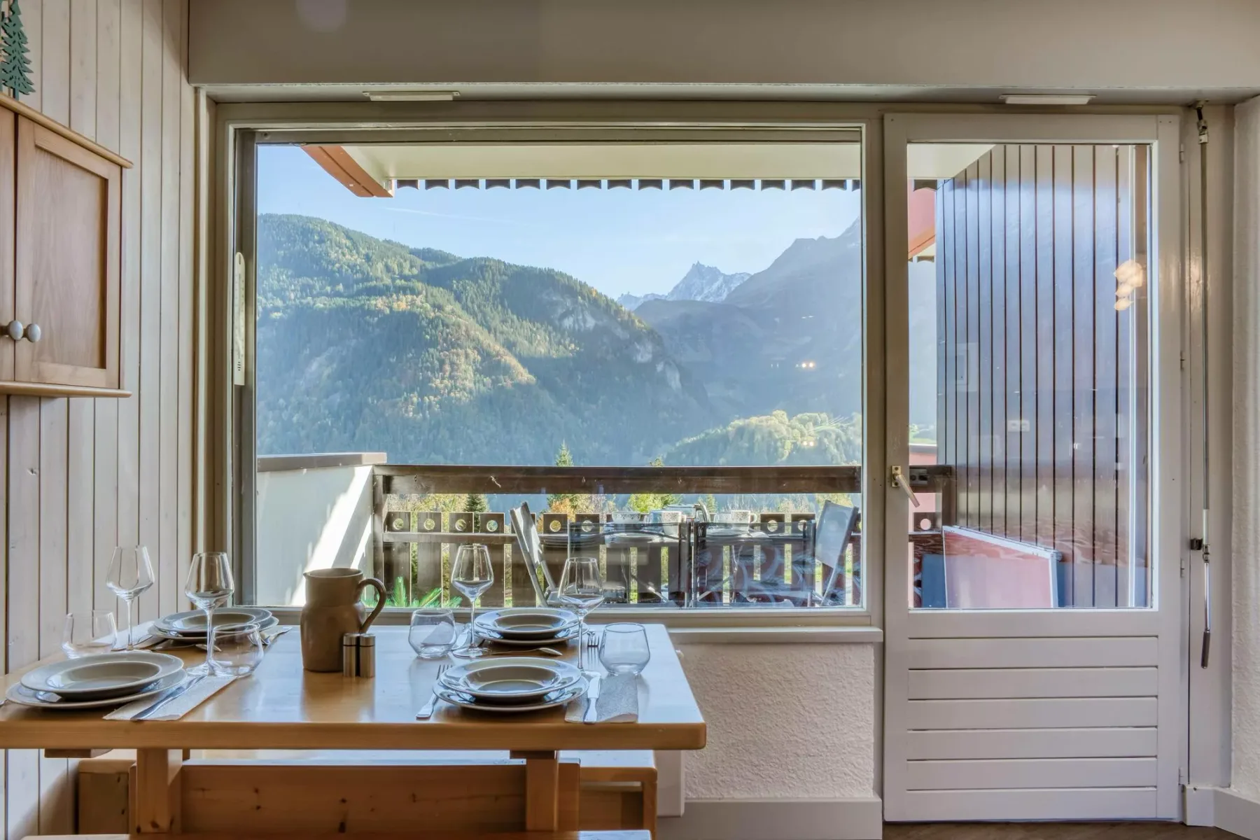 A dining table set for a meal faces a large window with mountain views.