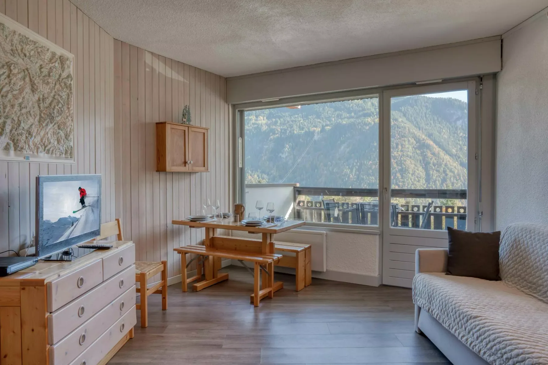 A bright living and dining area with a table beside large windows overlooking mountains.