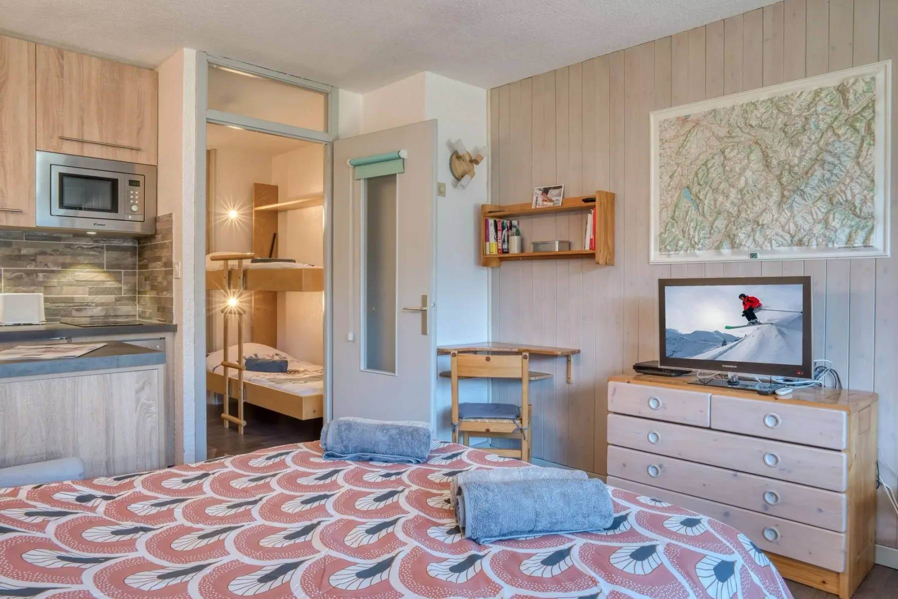 A bedroom with a patterned rug, a desk, and a dresser beneath a wall map.