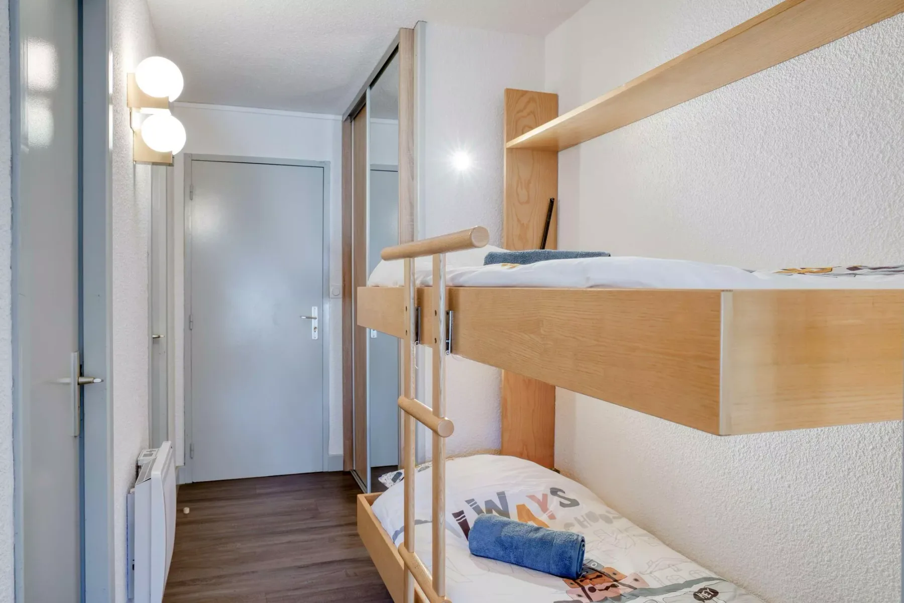 A narrow bedroom with wooden bunk beds and a hallway door.