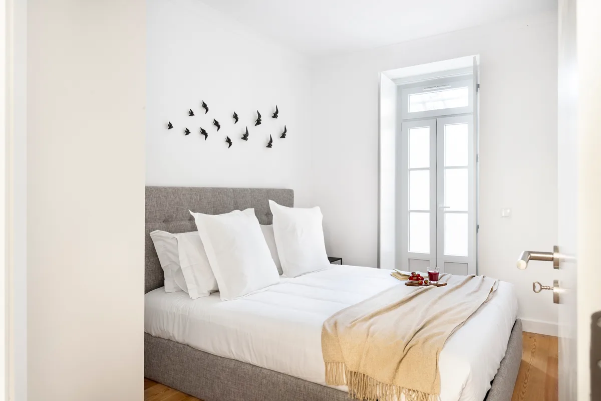Un dormitorio luminoso con una cama bien tendida y una ventana alta.