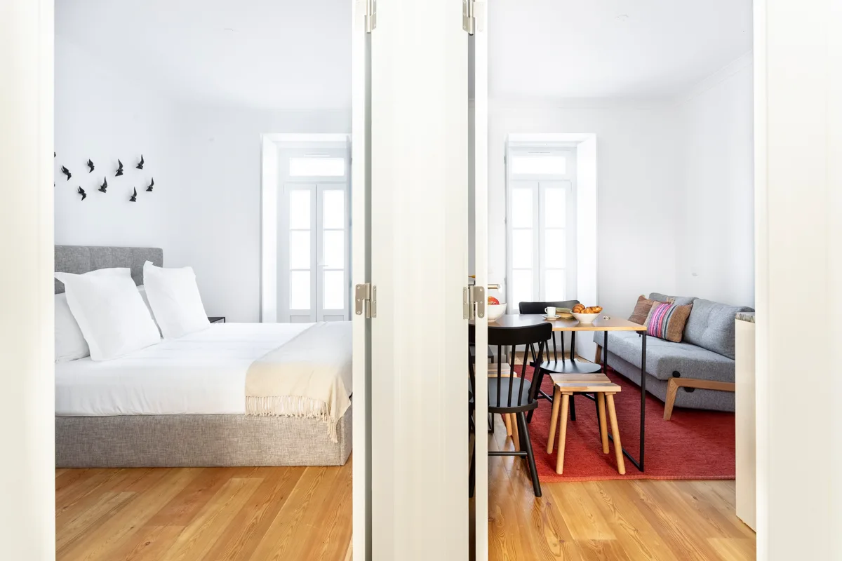 Un dormitorio luminoso y una zona de estar se ven a través de una puerta abierta.