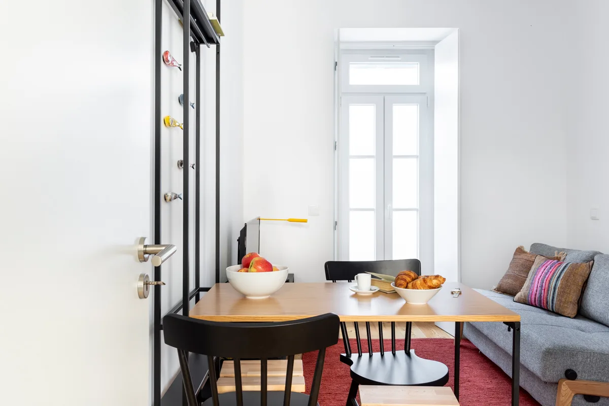 Un comedor luminoso con una mesa junto a un sofá y ventanas altas.