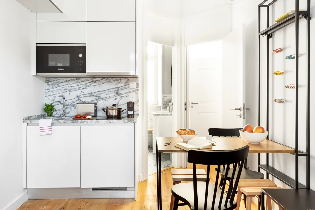 Una cocina y comedor luminosos con armarios blancos y una mesa de madera.