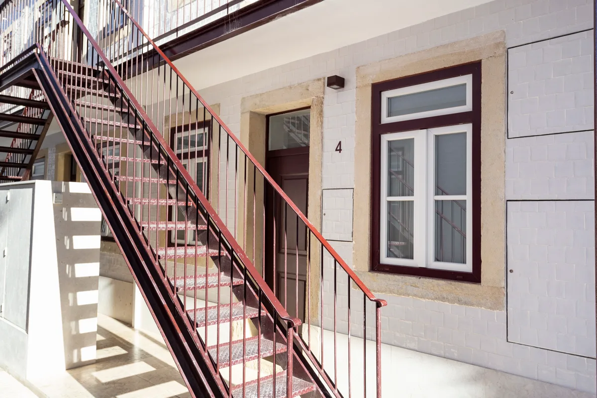 Una escalera exterior junto a una pared de azulejos blancos con una ventana.