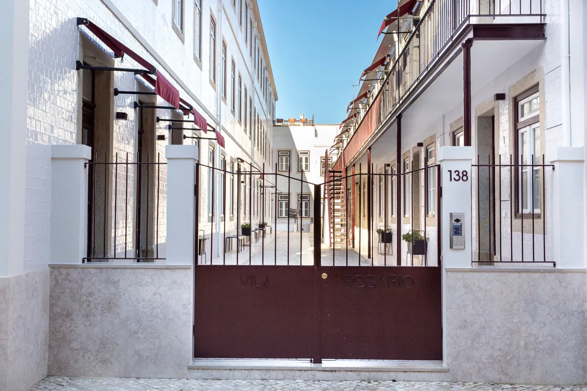 Una entrada con portón entre edificios blancos, con balcones que dan al patio.