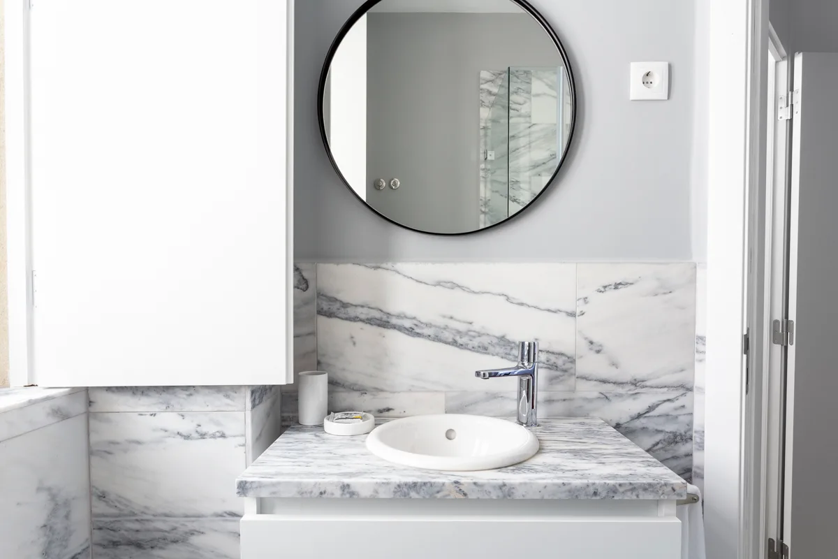 Un lavabo de baño con espejo redondo y un lavabo blanco sobre encimera.