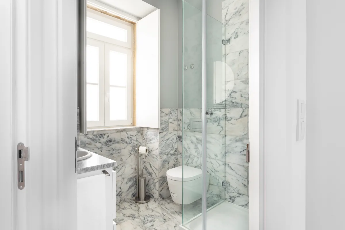 Un baño luminoso con una ducha de cristal junto a una ventana.