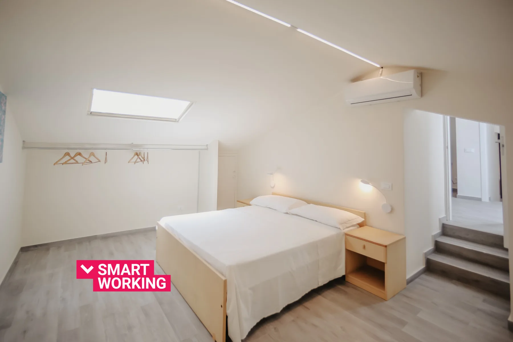 Un dormitorio luminoso con cama doble, mesita de noche y espacio abierto para colgar ropa.