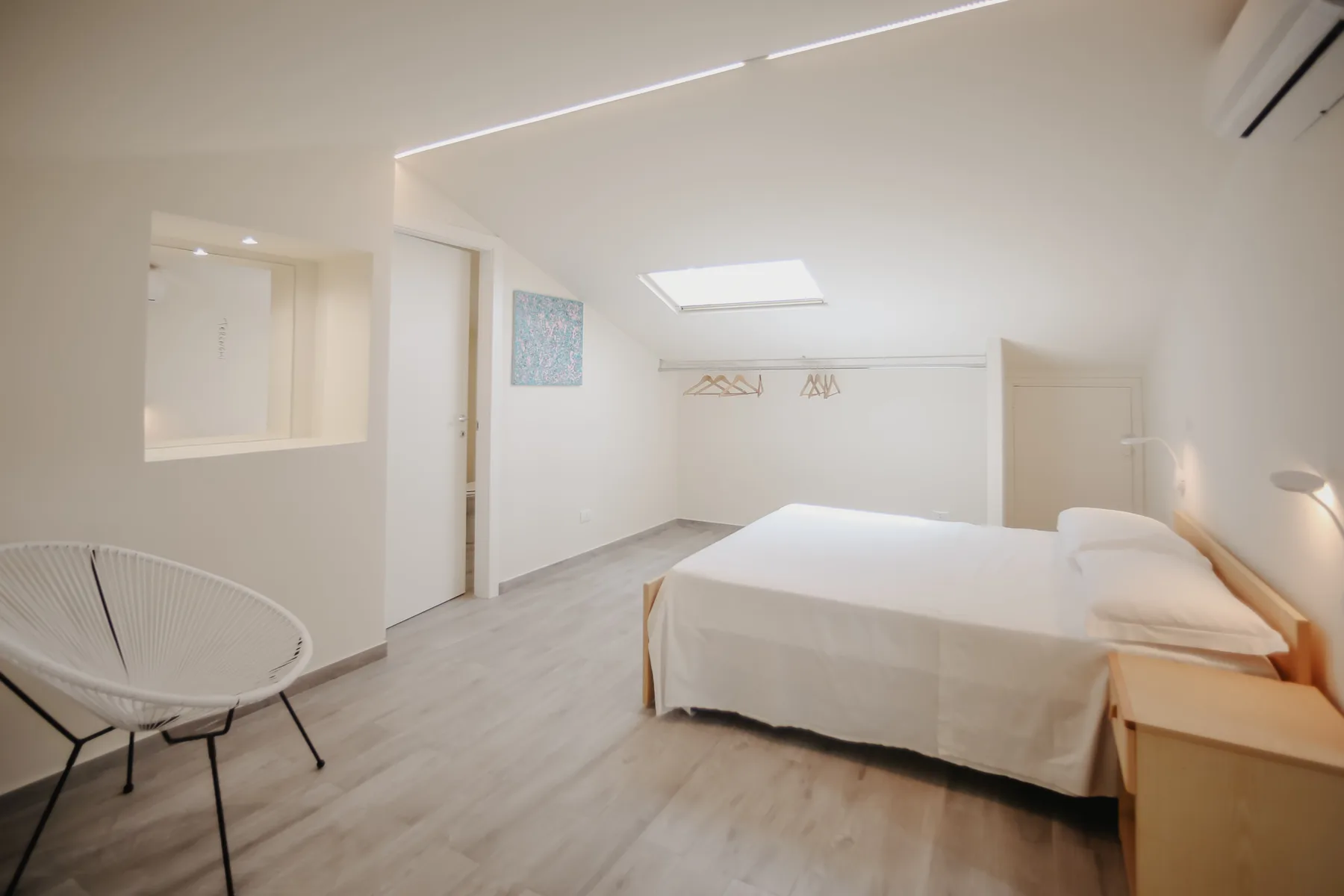Un dormitorio luminoso con una cama, una claraboya y una silla tejida.