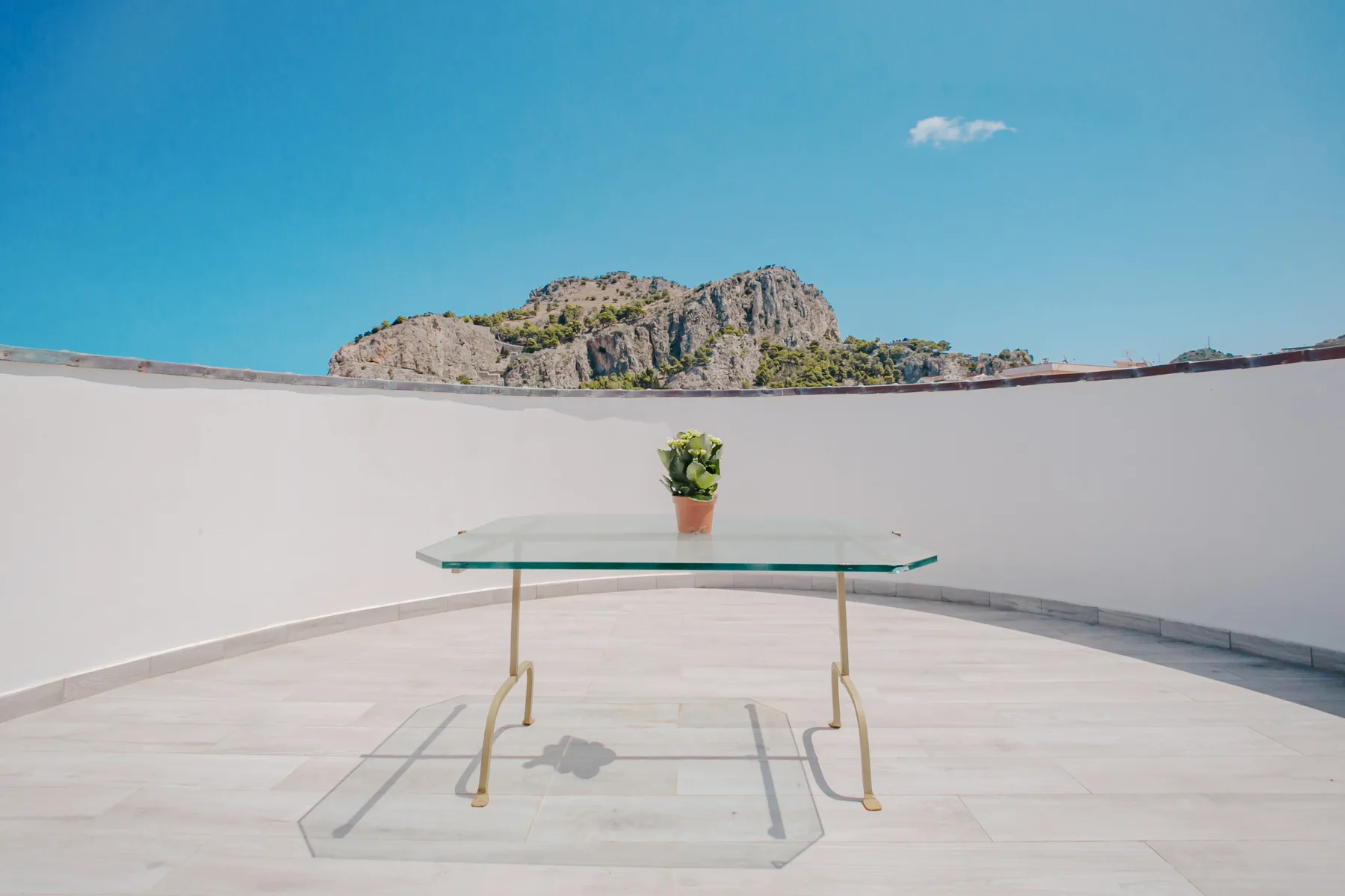 A sunlit terrace with a glass table and a small potted plant.