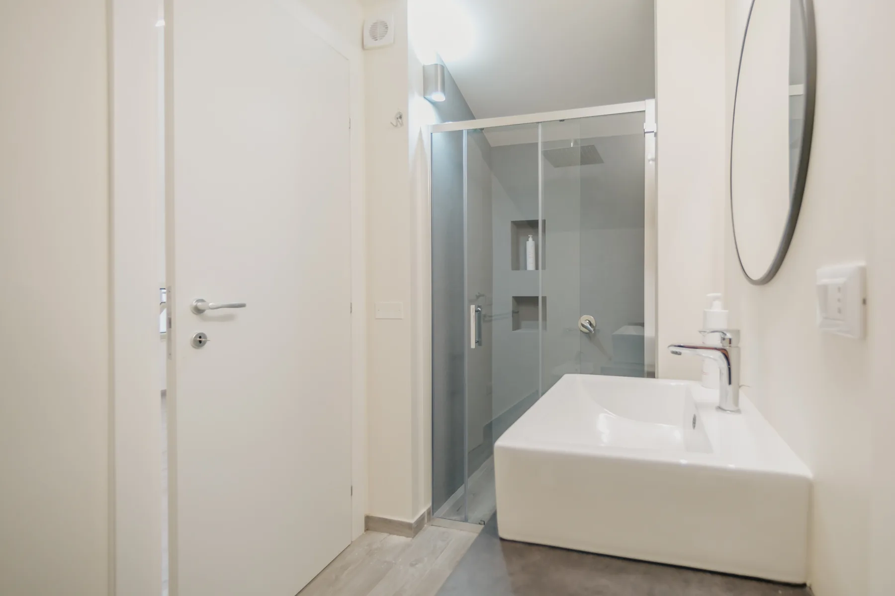 Un baño luminoso con una ducha de vidrio y un lavabo blanco amplio.
