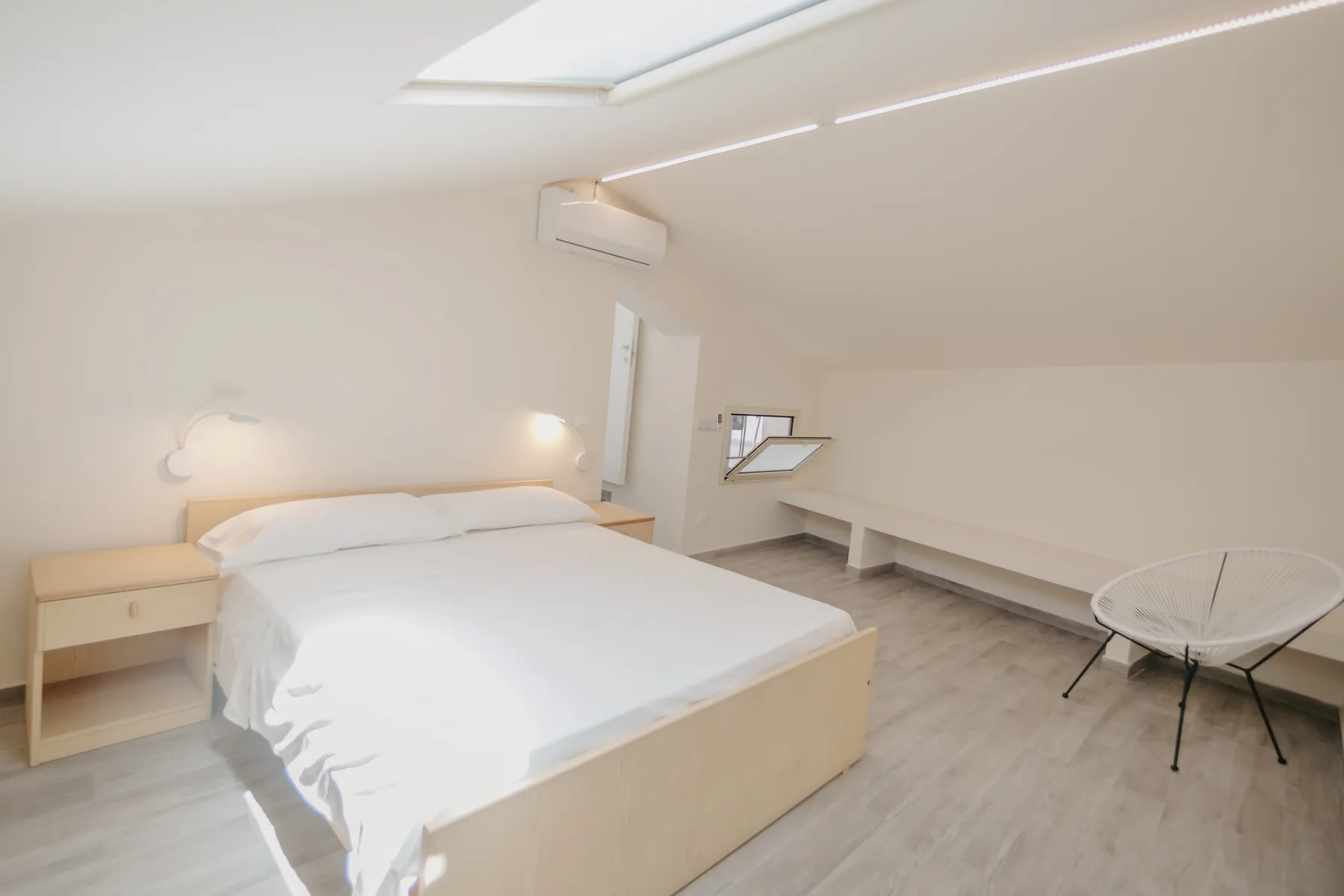 Un dormitorio luminoso con una cama, estantes bajos empotrados y una claraboya.