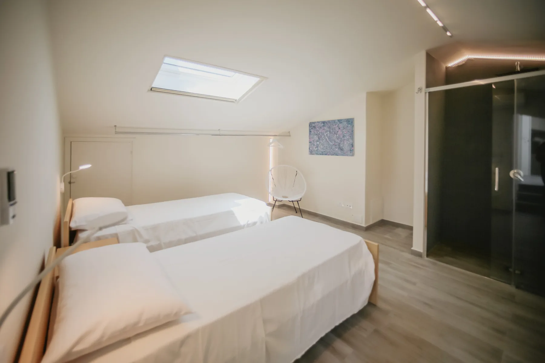 Un dormitorio con dos camas, una claraboya y una ducha de vidrio oscuro.
