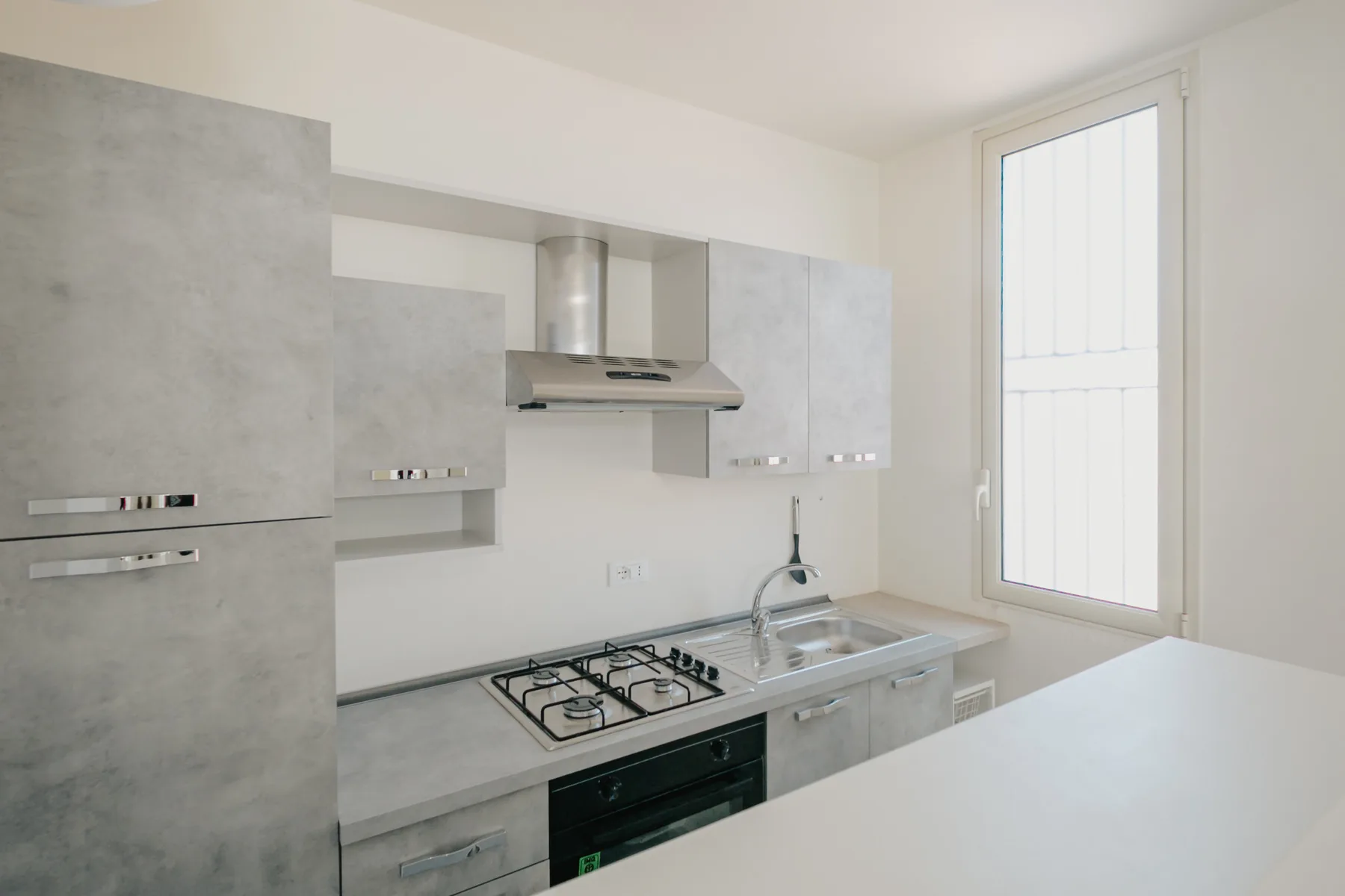 A bright kitchen with gray cabinets, a cooktop, and a large window.