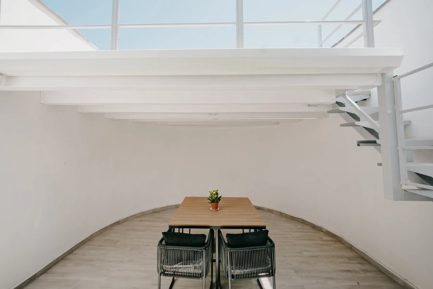 Un comedor luminoso bajo un techo de vidrio, con una mesa de madera y asientos.