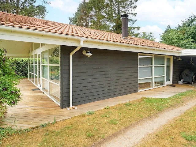 A dark-sided house with a tiled roof and a wooden deck.