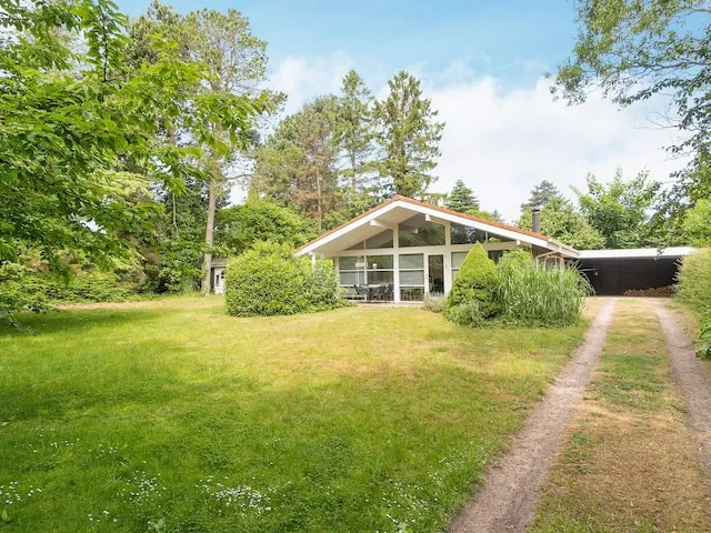 A house stands in a grassy yard beside a driveway and leafy trees.