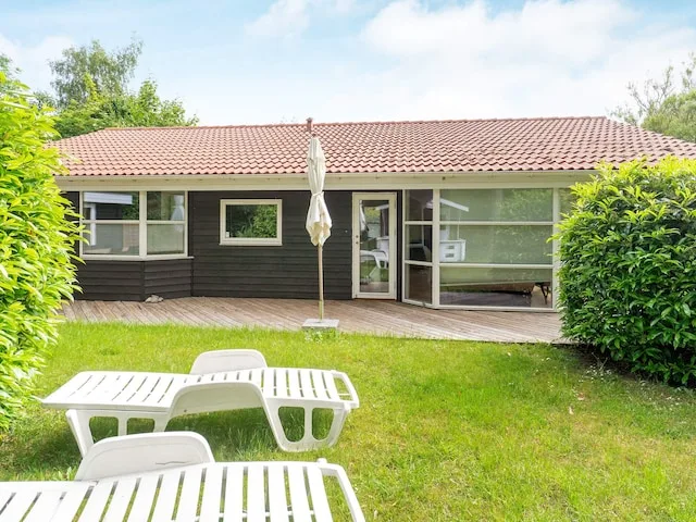 A low house with a tiled roof faces a grassy yard with outdoor seating.