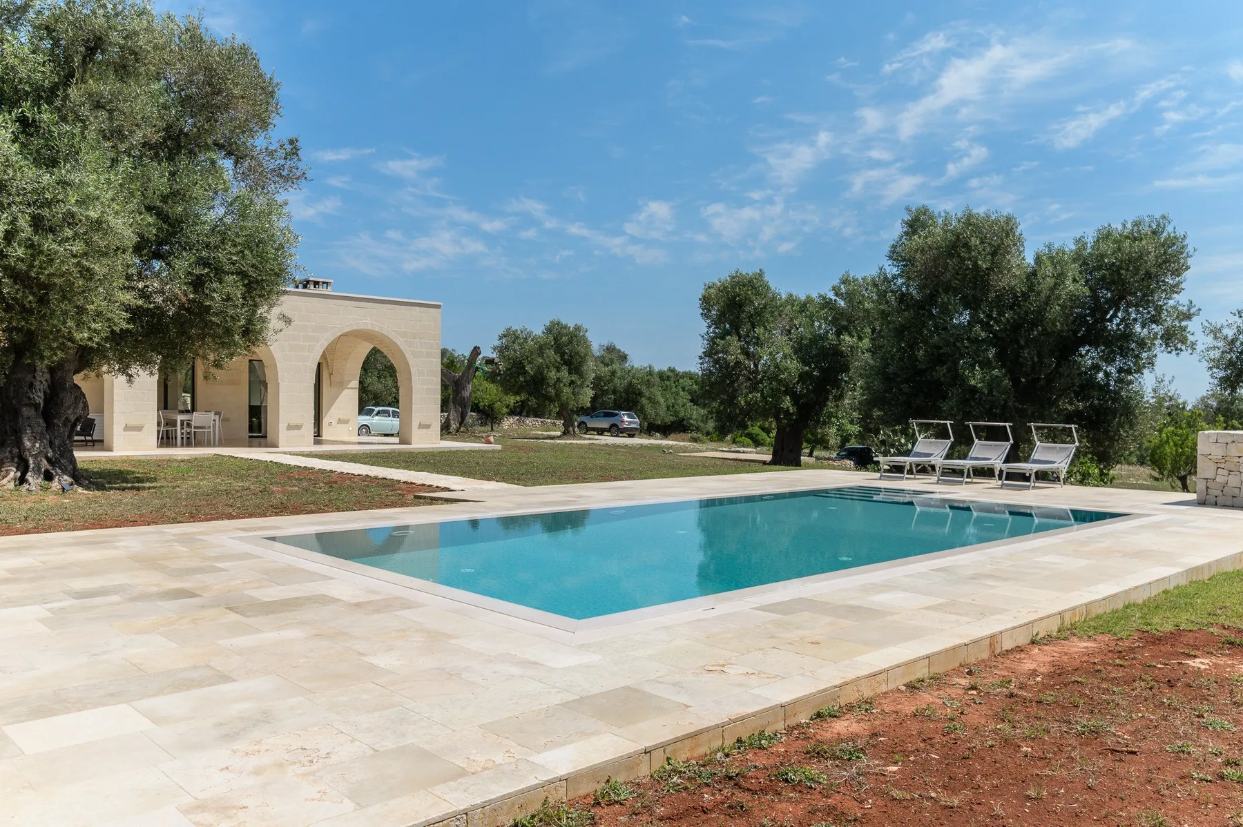 An outdoor swimming pool beside a stone patio and a small arched building.