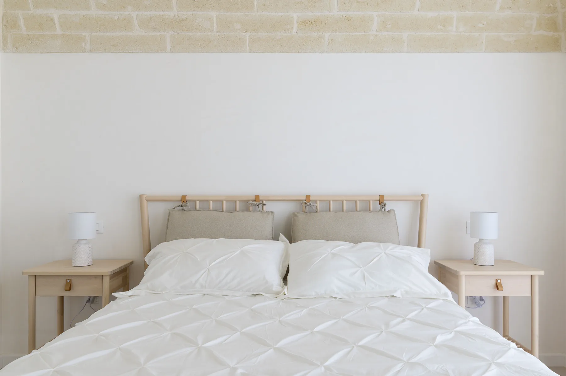A bedroom with a bed dressed in white bedding and matching bedside tables.