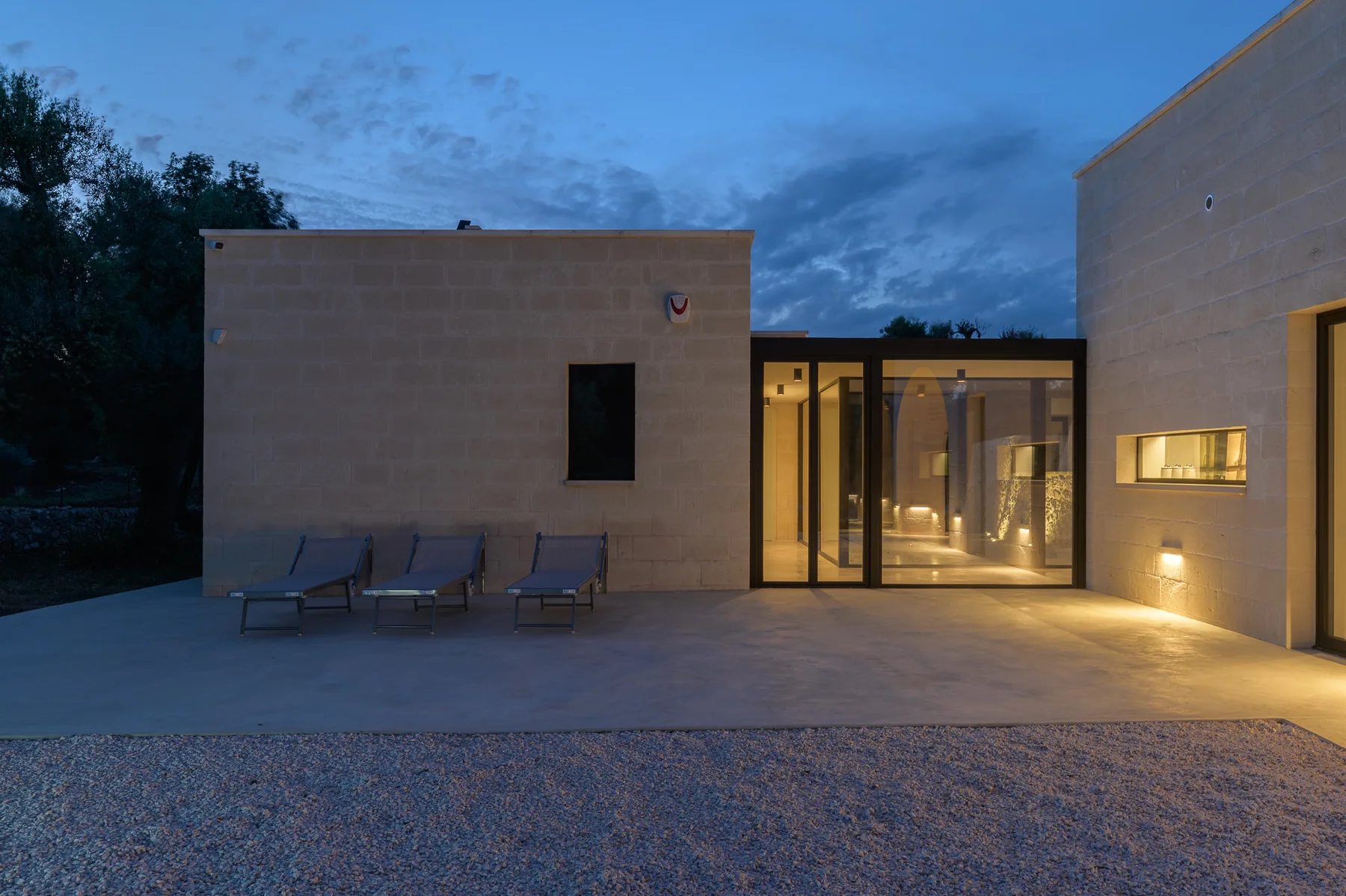 A modern building courtyard at dusk, with outdoor seating beside illuminated glass doors.