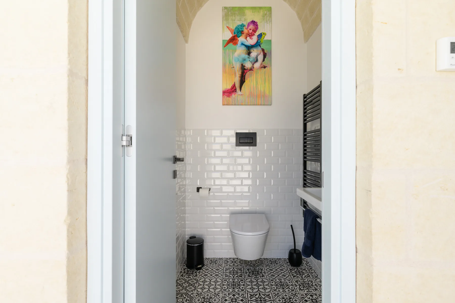 A tiled bathroom with a toilet, patterned floor, and colorful wall art.