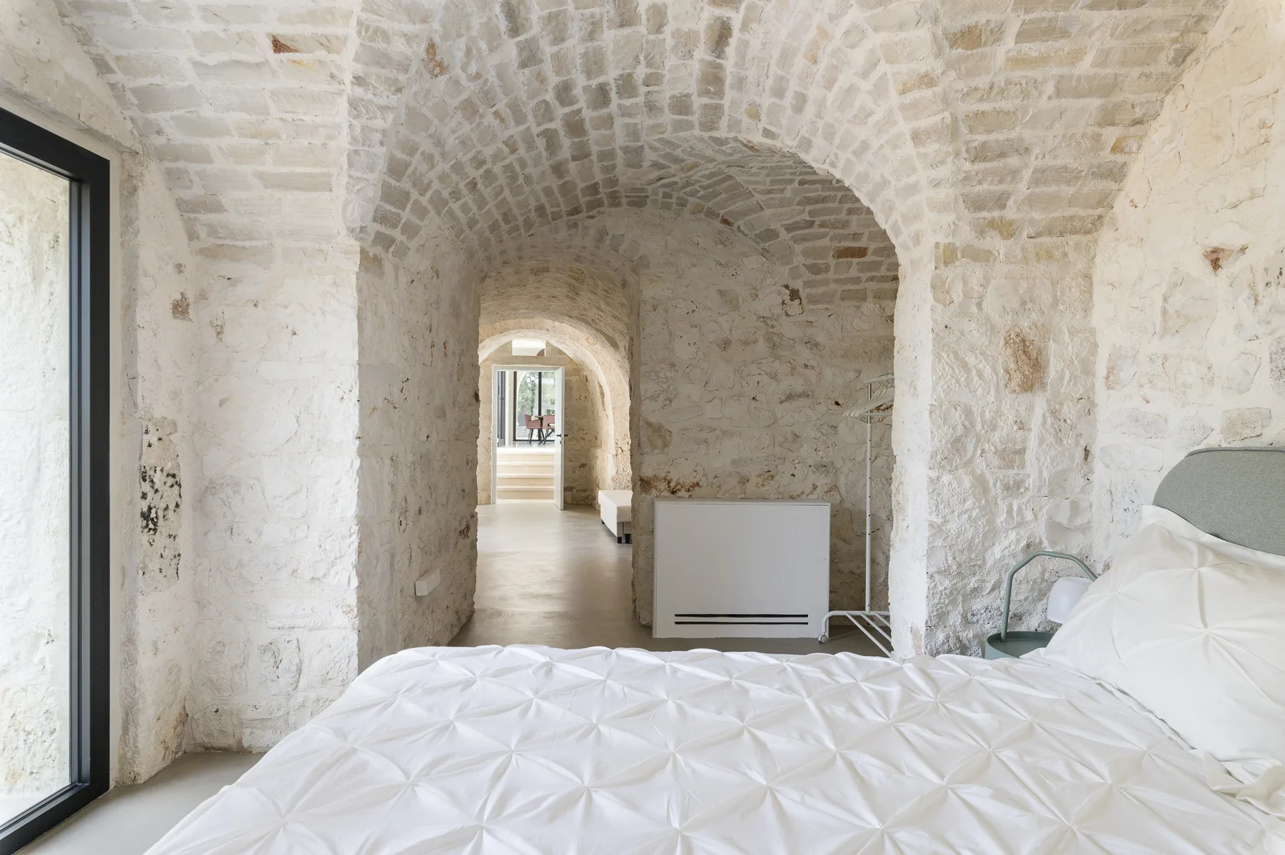 A bedroom with a white bed beneath a vaulted stone ceiling.