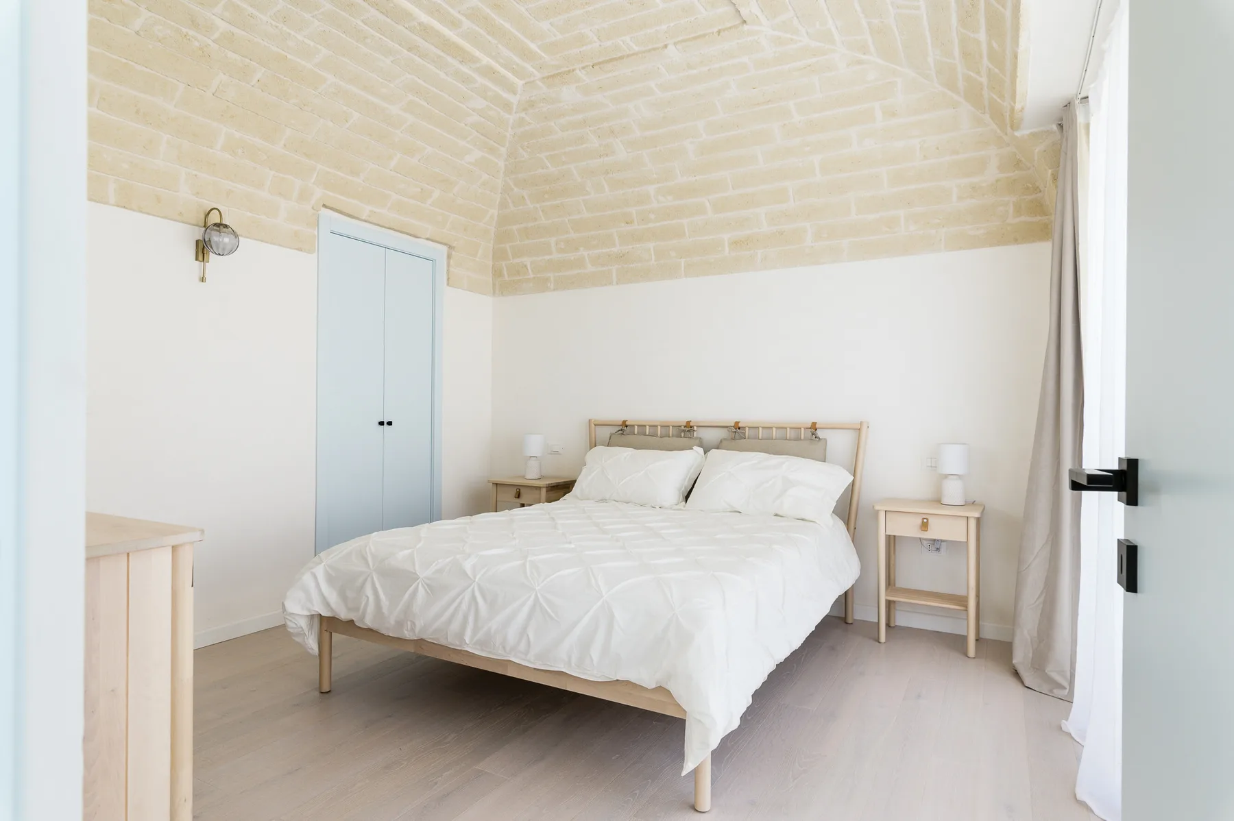 A bright bedroom with a bed dressed in white linens and pale brick walls.