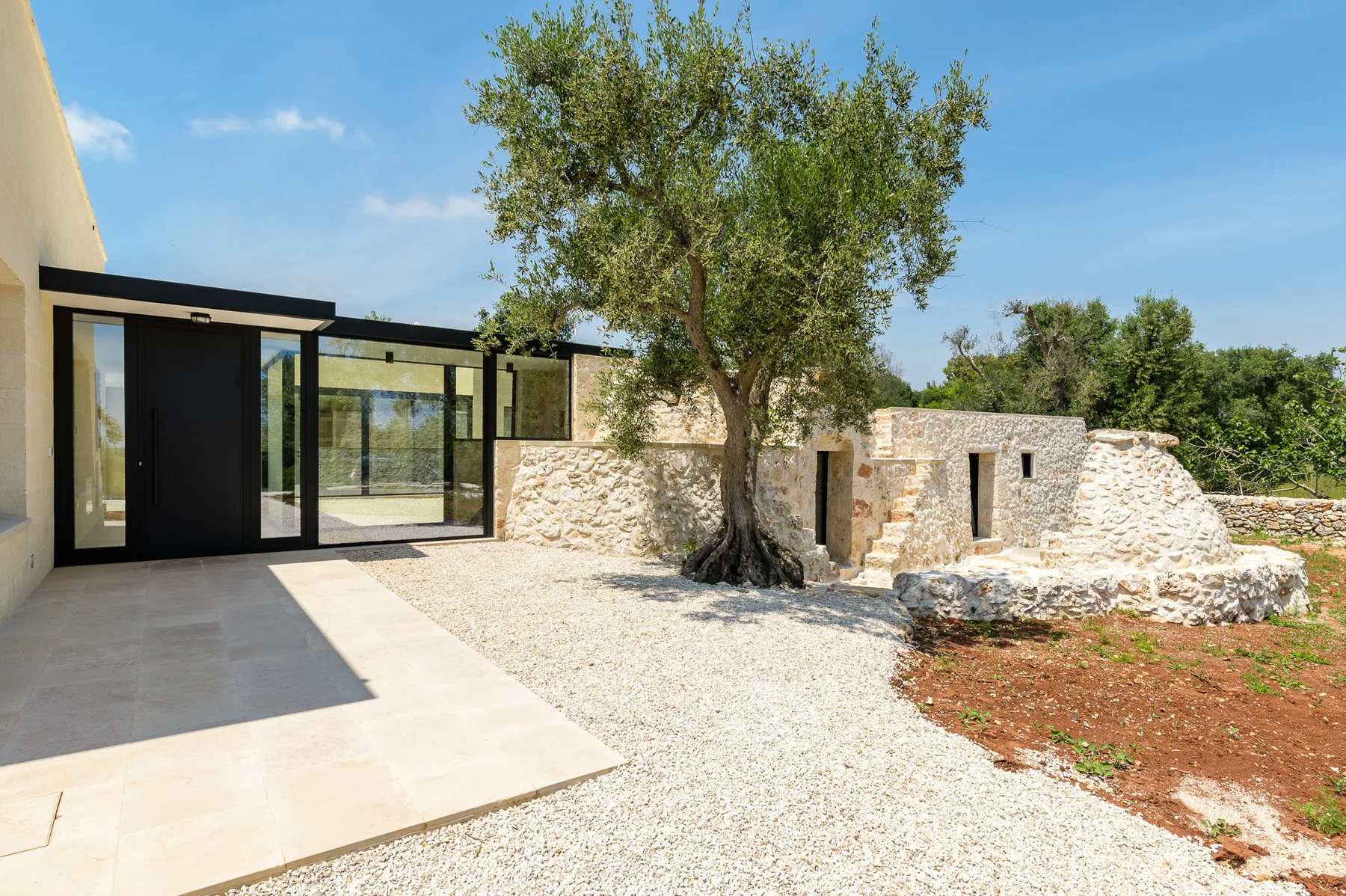 A sunlit courtyard with a large tree, pale gravel, and stone walls.