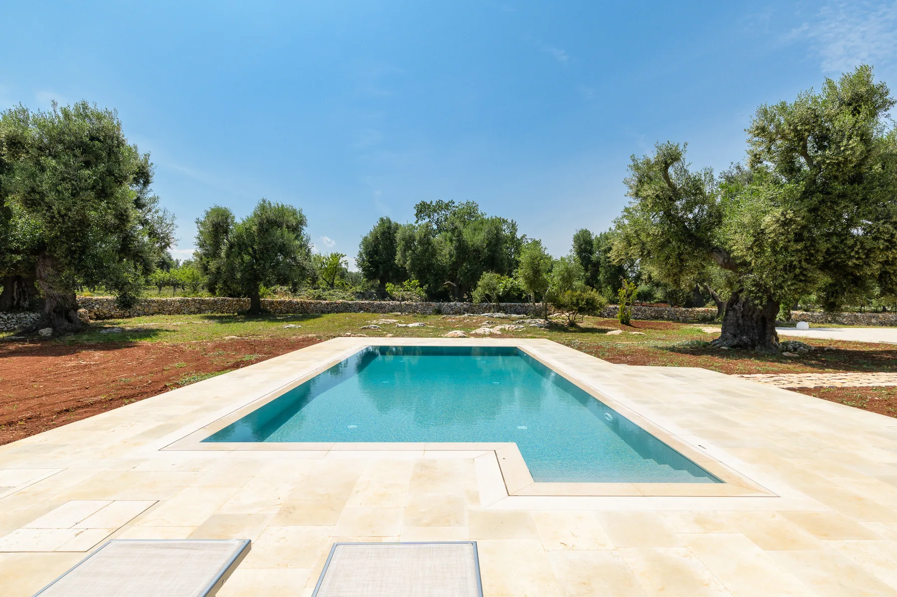 A swimming pool sits in a broad pale stone terrace among trees.
