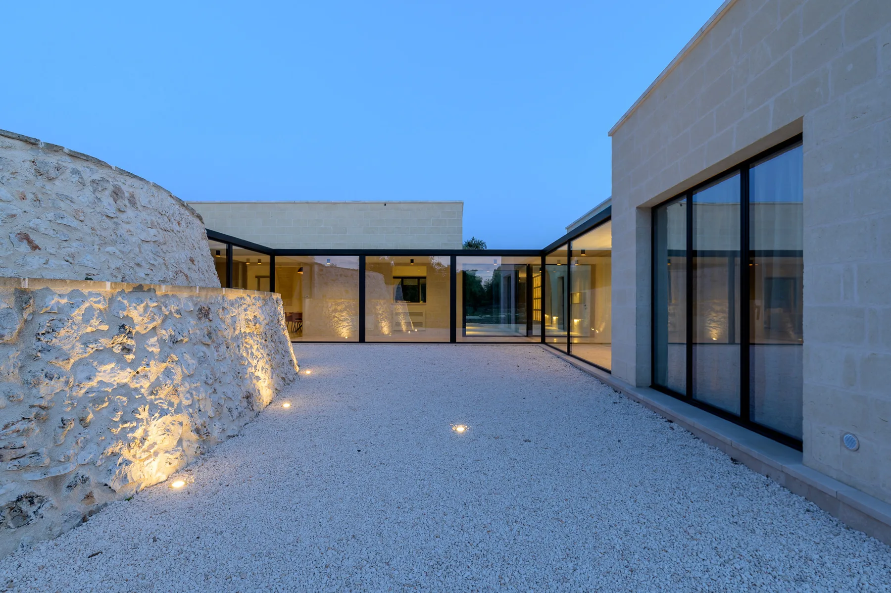 A modern courtyard with pale gravel, stone walls, and glass doors.