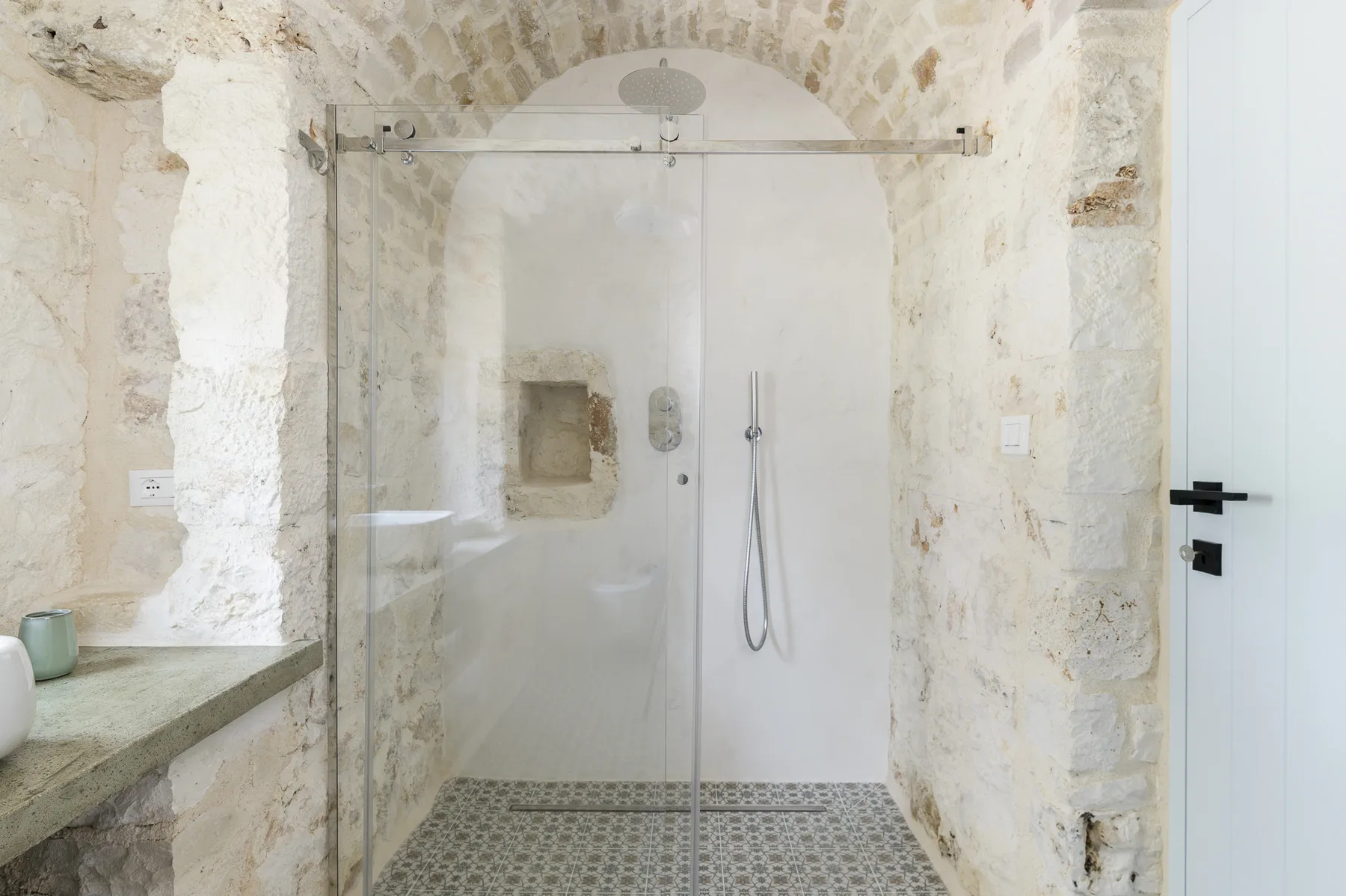 A stone bathroom with a glass shower and a built-in wall niche.