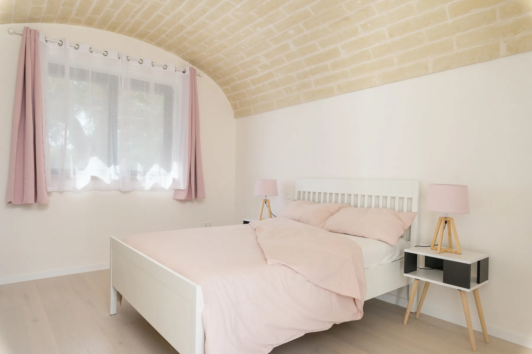 A bedroom with a pale bed beneath a curved brick ceiling.