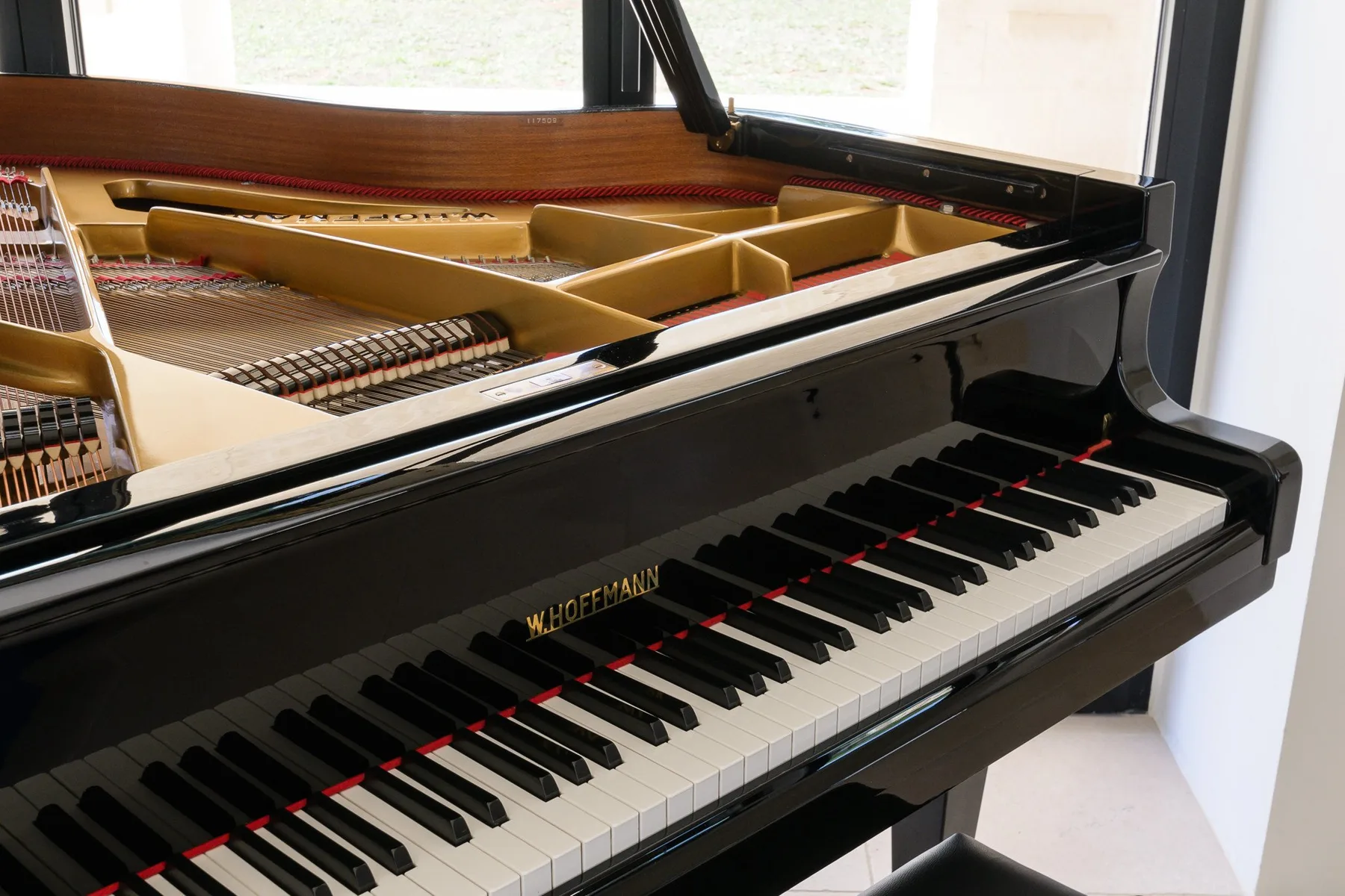 An open grand piano stands beside a bright window.