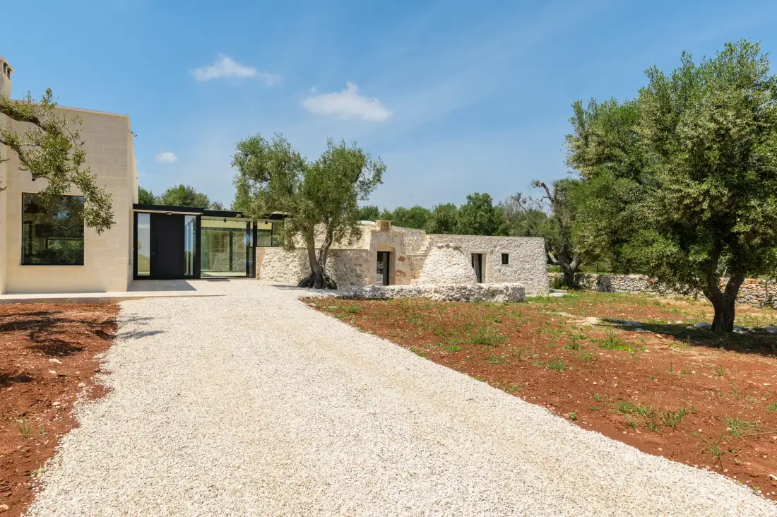 A modern building and stone structures stand beside a broad gravel driveway.