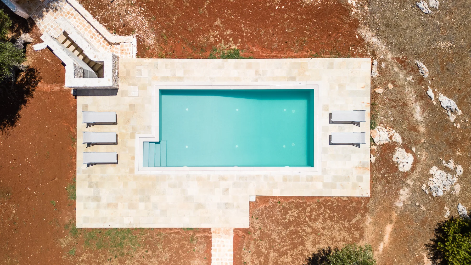 An overhead view of a rectangular swimming pool set in a pale paved area.
