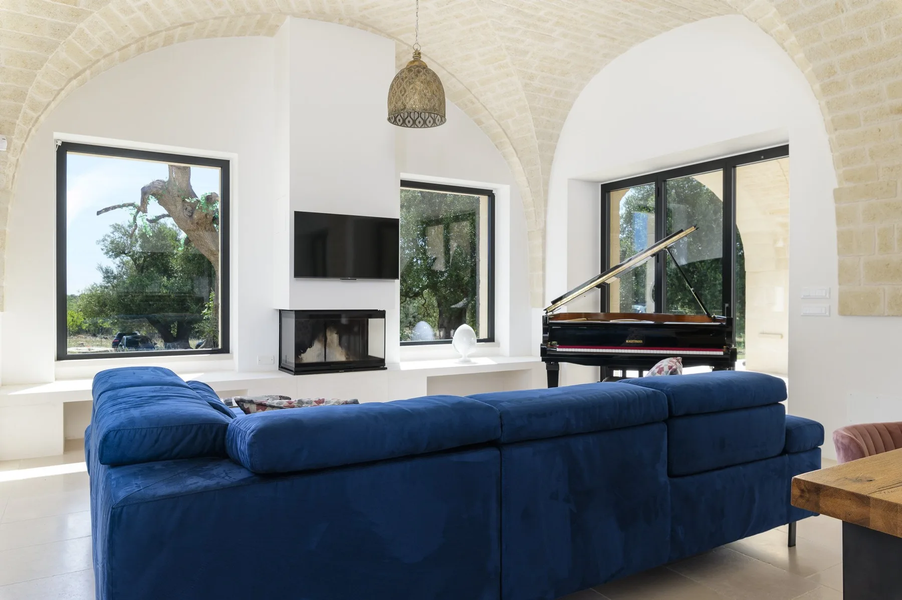 A vaulted living room with blue seating, a fireplace, and a piano.
