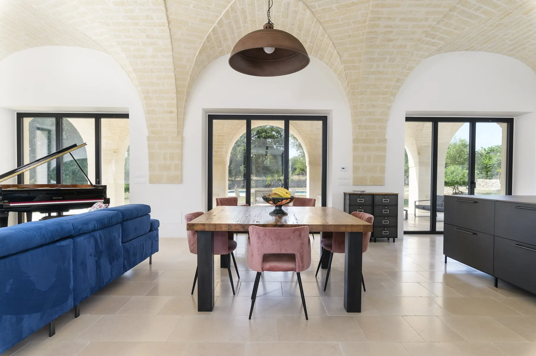 A bright dining and living area with a table, blue seating, and a piano.