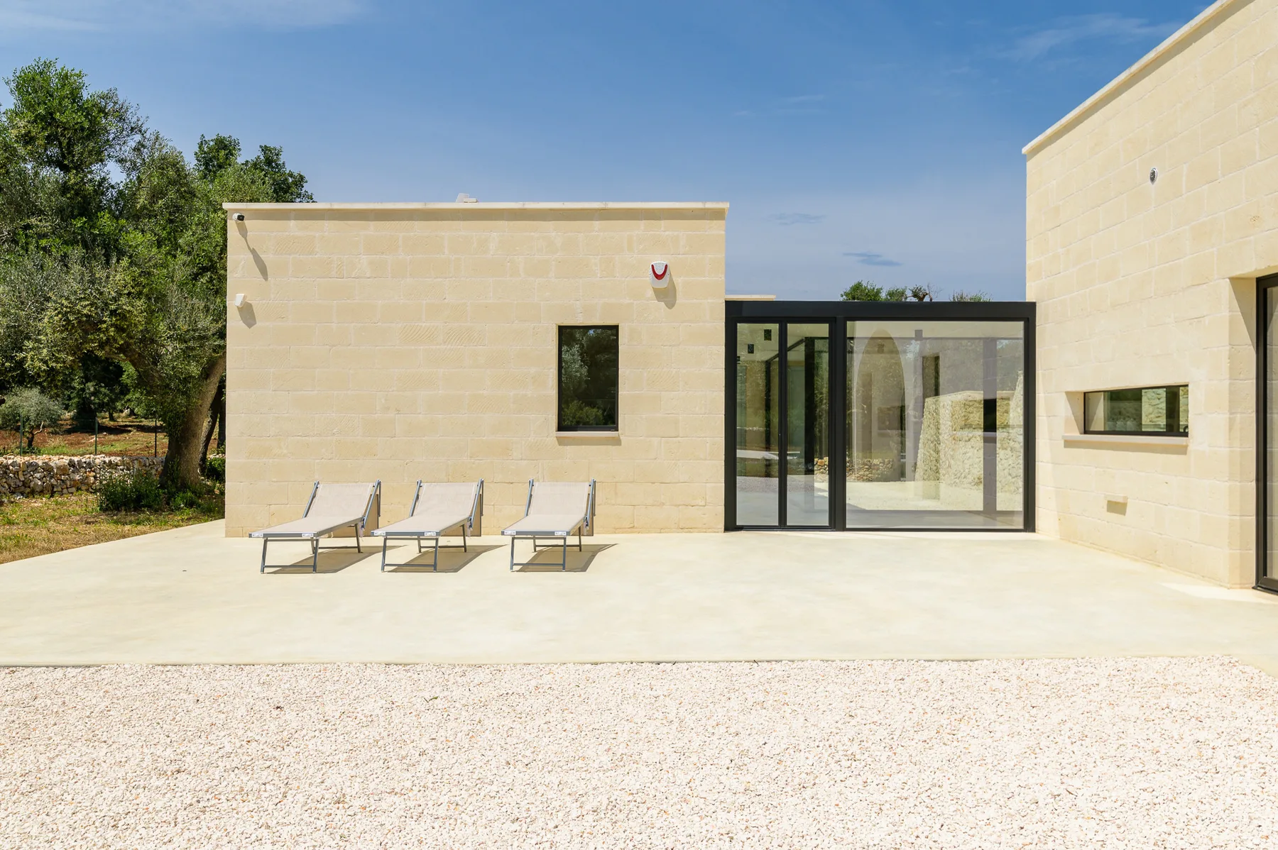 A sunlit patio beside a modern building features three reclining lounge chairs.