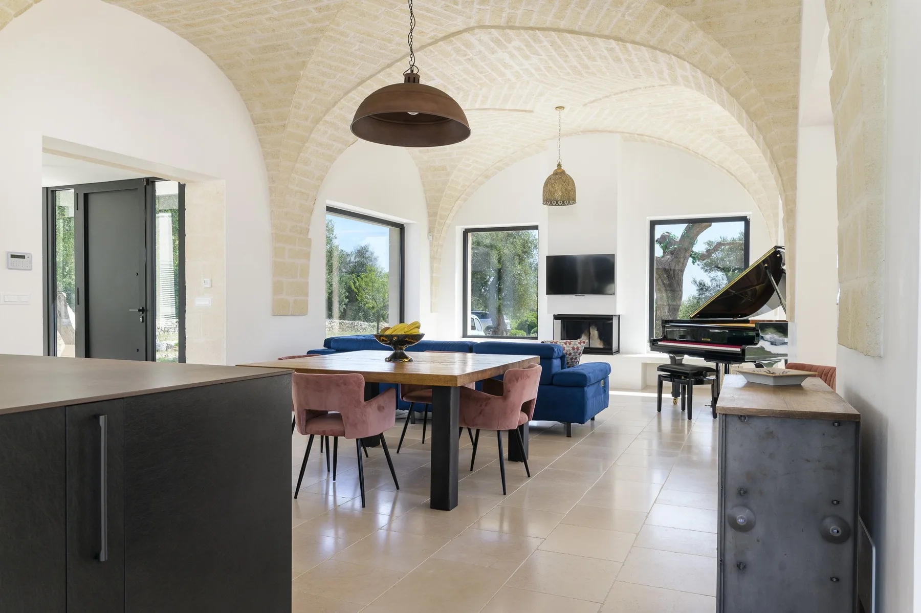 A bright vaulted living and dining room with a grand piano and table.