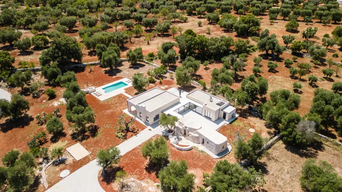 An aerial view of a modern house and swimming pool amid a tree-filled landscape.