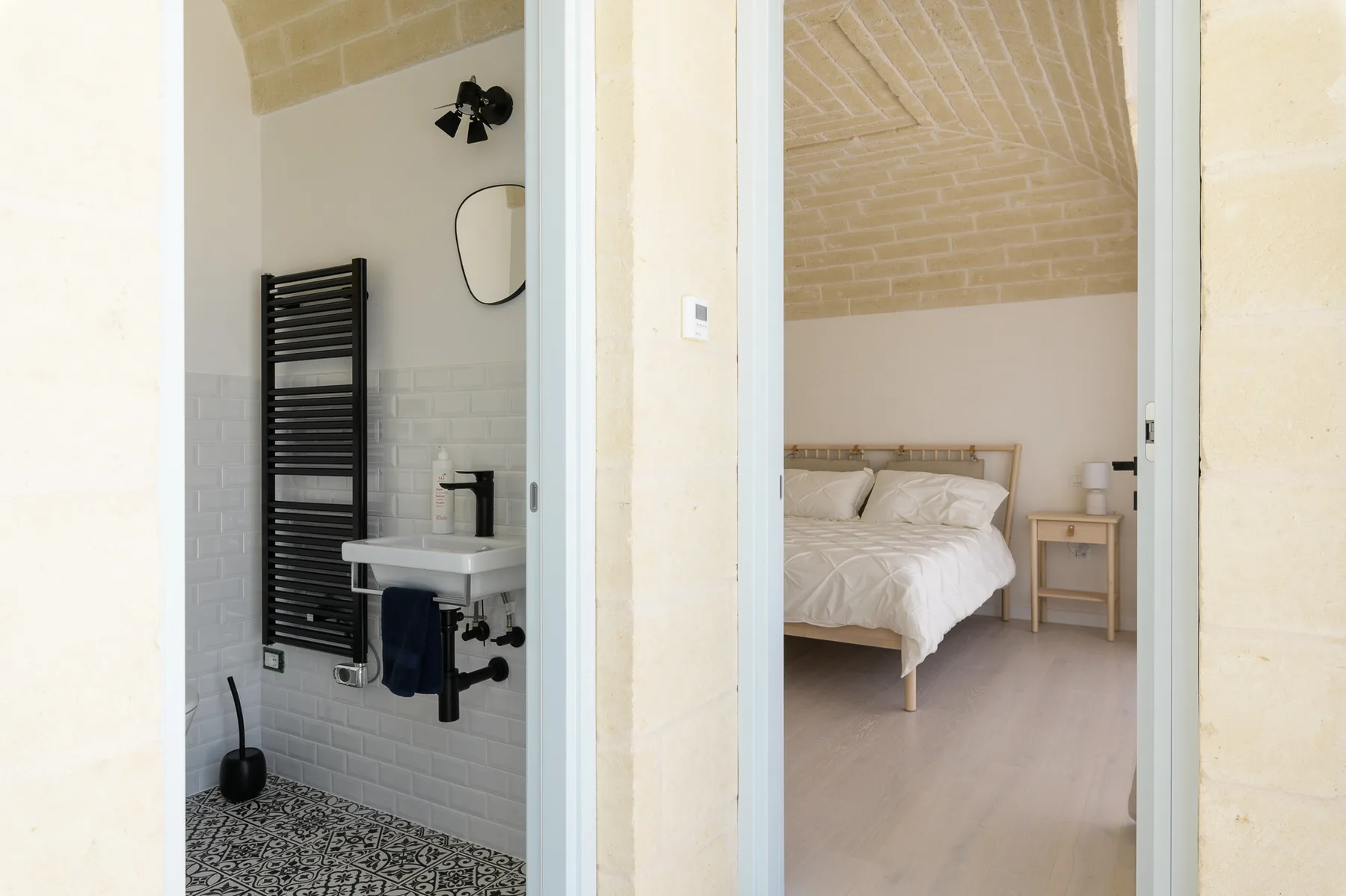 A bedroom with a bed is visible beside a bathroom with a sink and towel radiator.