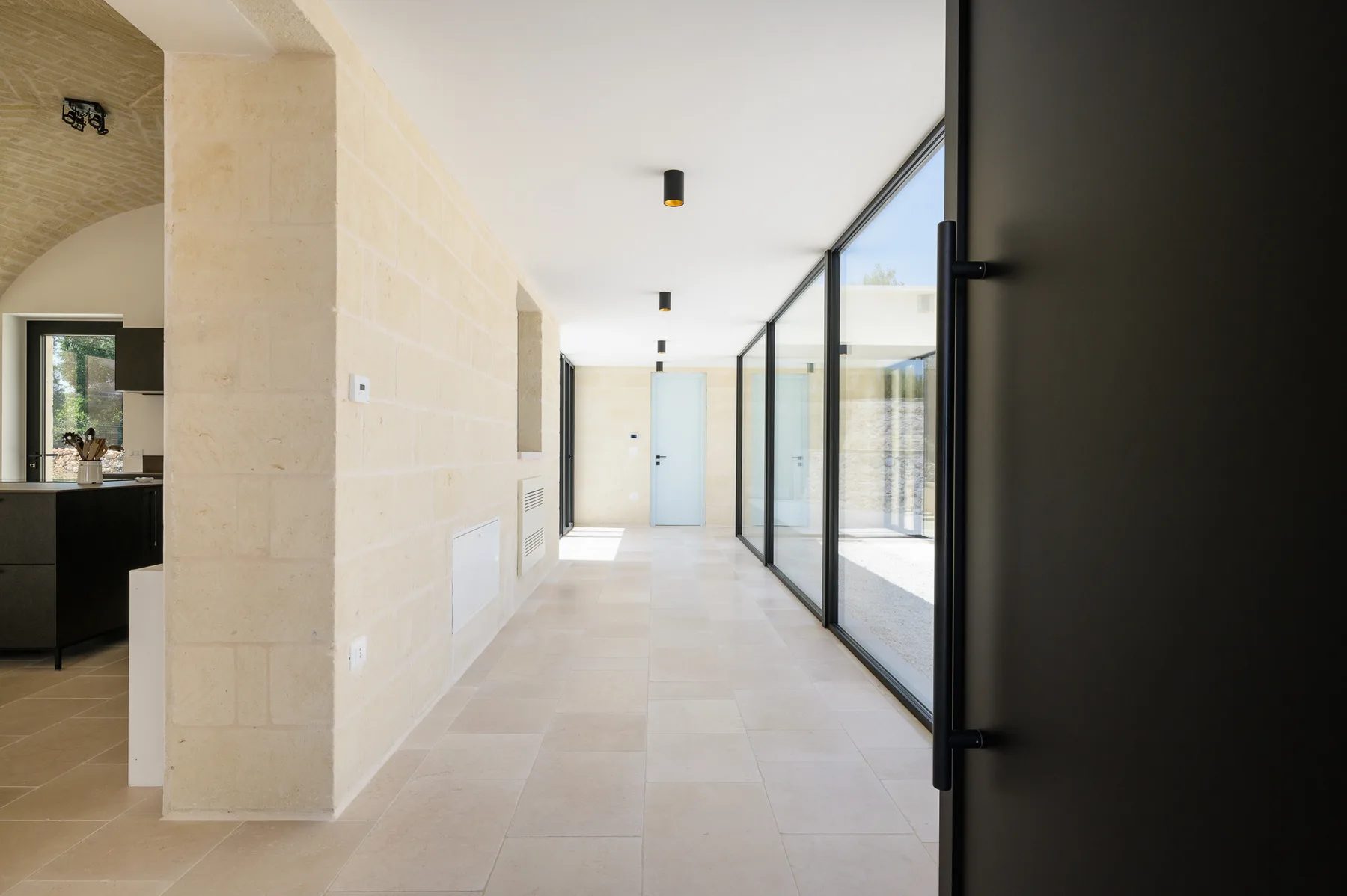 A bright interior hallway with pale stone walls and glass doors along one side.