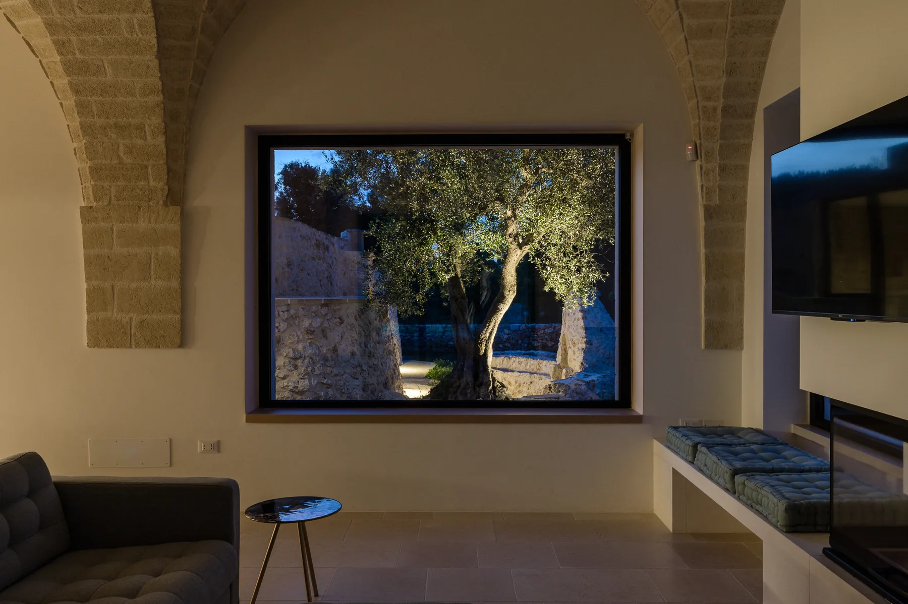 A living room with a large window overlooking a tree.