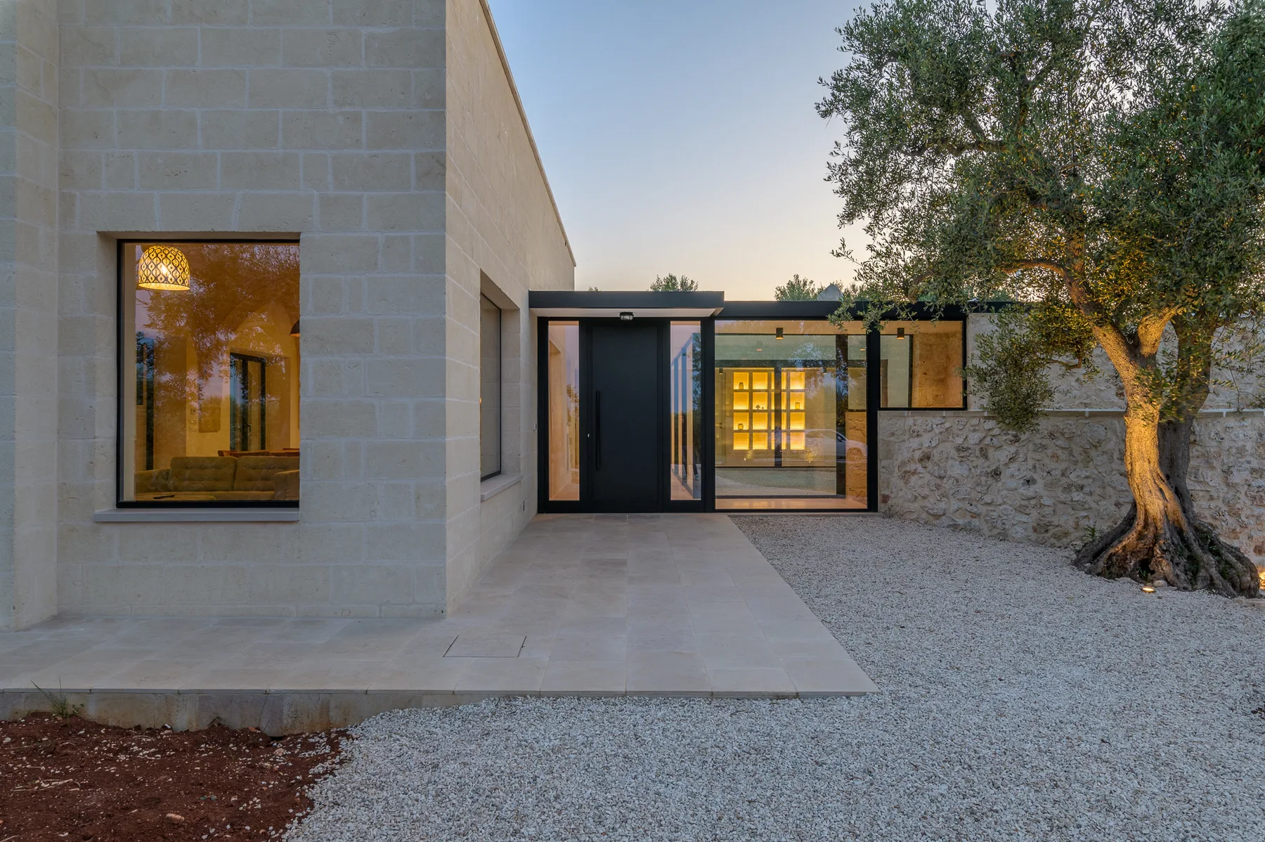 A modern building exterior opens onto a gravel courtyard beside a tree.