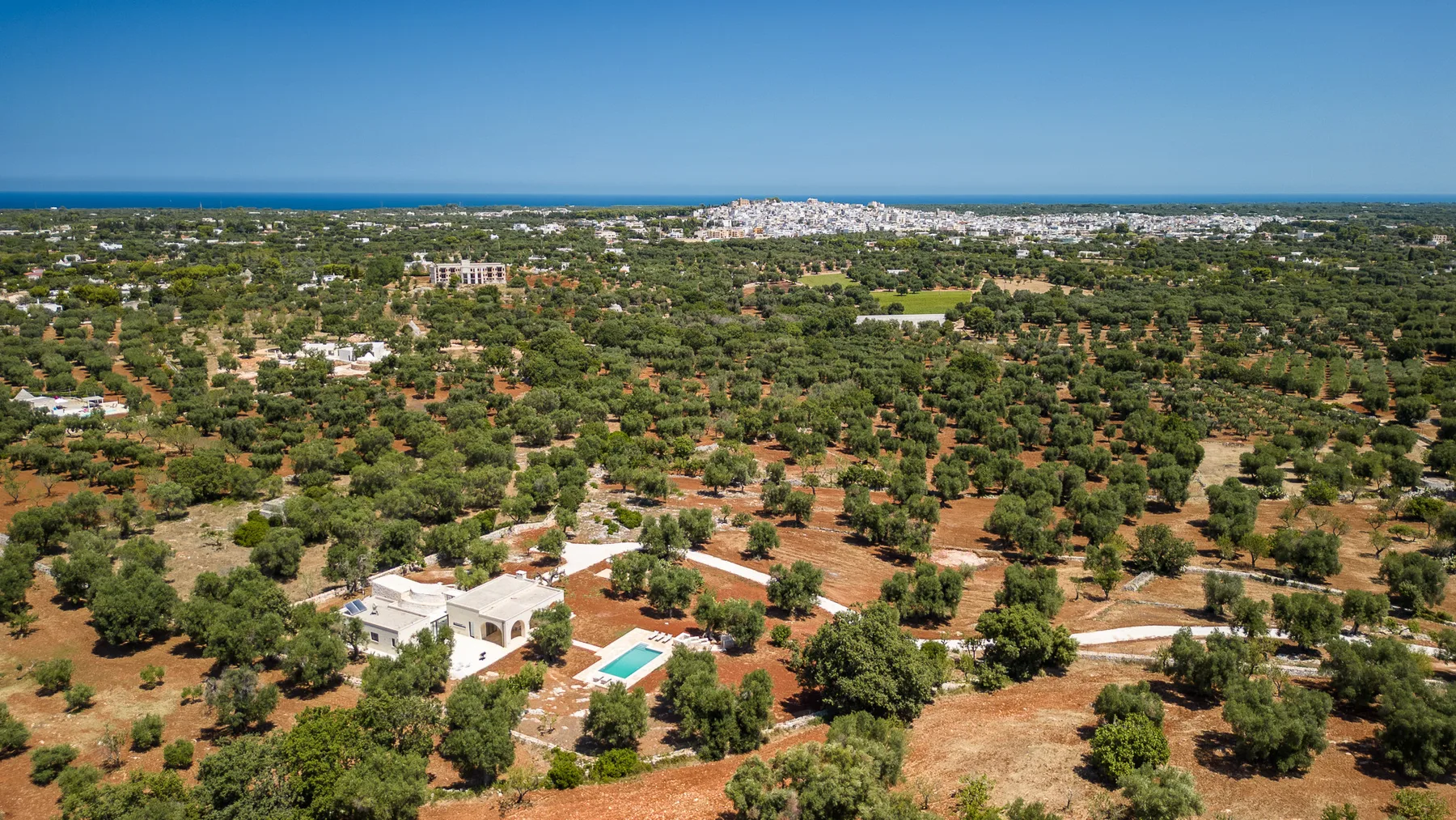 An aerial view shows scattered homes and greenery stretching toward the distant coast.
