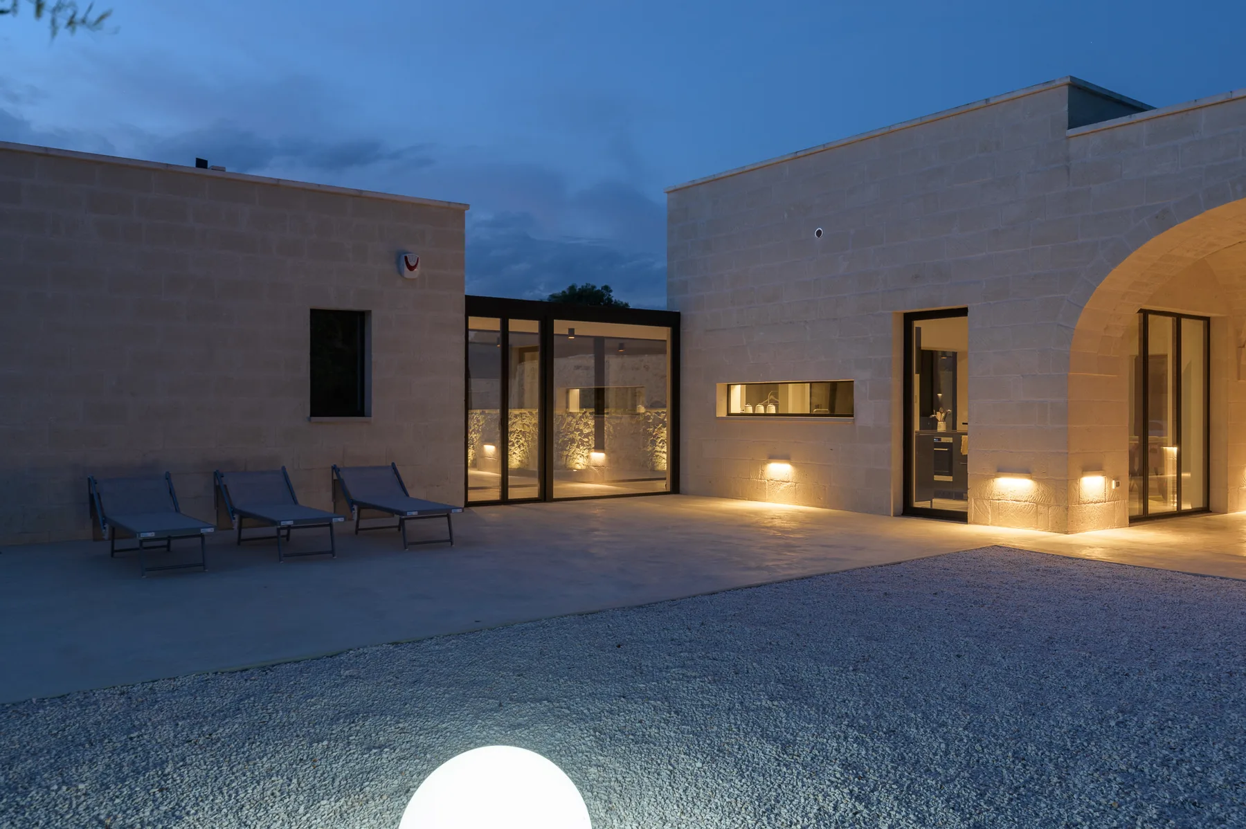 A modern courtyard at dusk, with outdoor seating and illuminated glass doors.