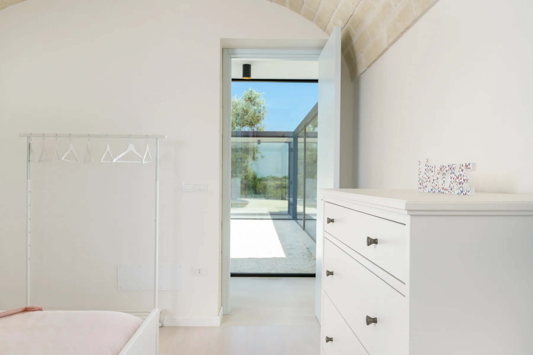 Bright bedroom with a white dresser beside an open doorway to a glass patio.